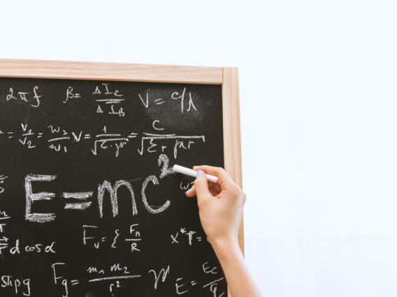 Photo of a hand writing an equation on a chalkboard